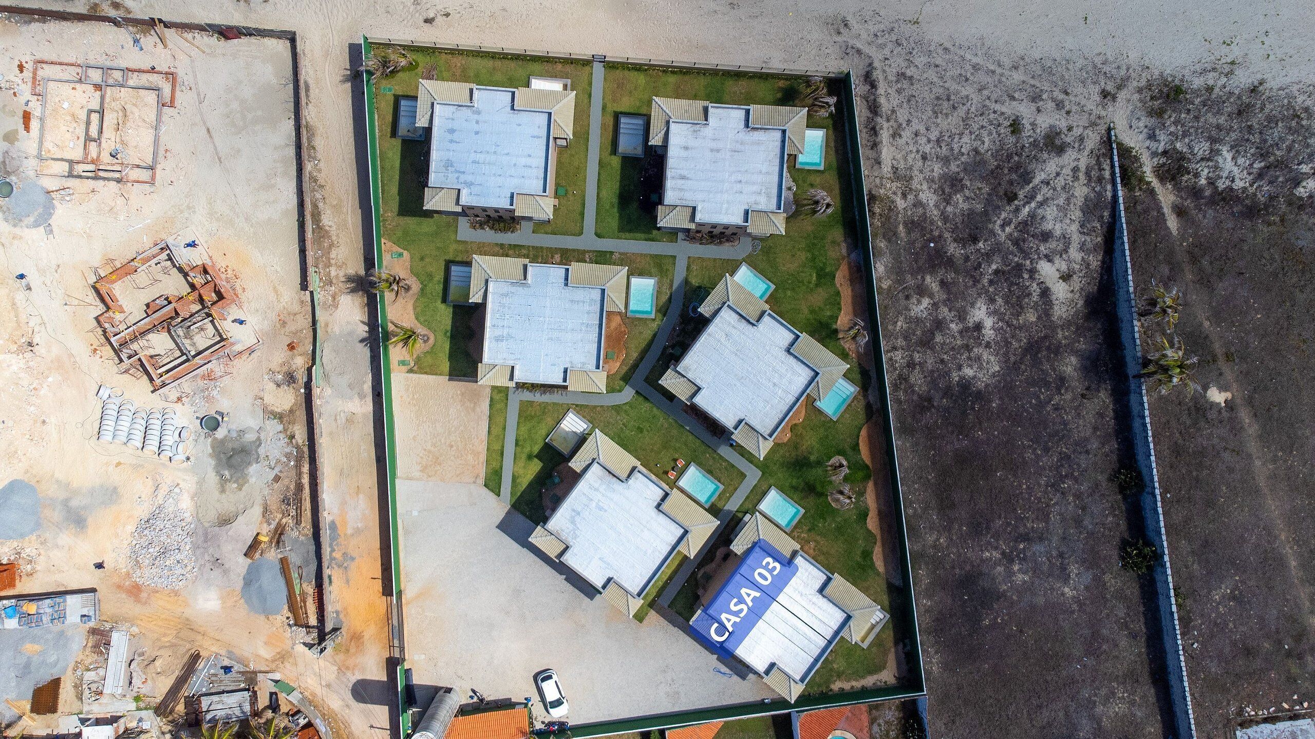 Vista aérea de un complejo residencial con varias casas, cada una con un diseño de techo diferente y una piscina.