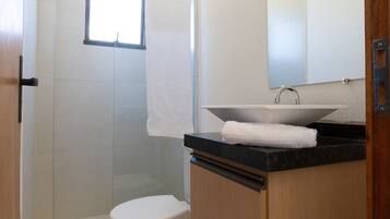 A bathroom with a toilet, a sink with a mirror above it, and a shower area.