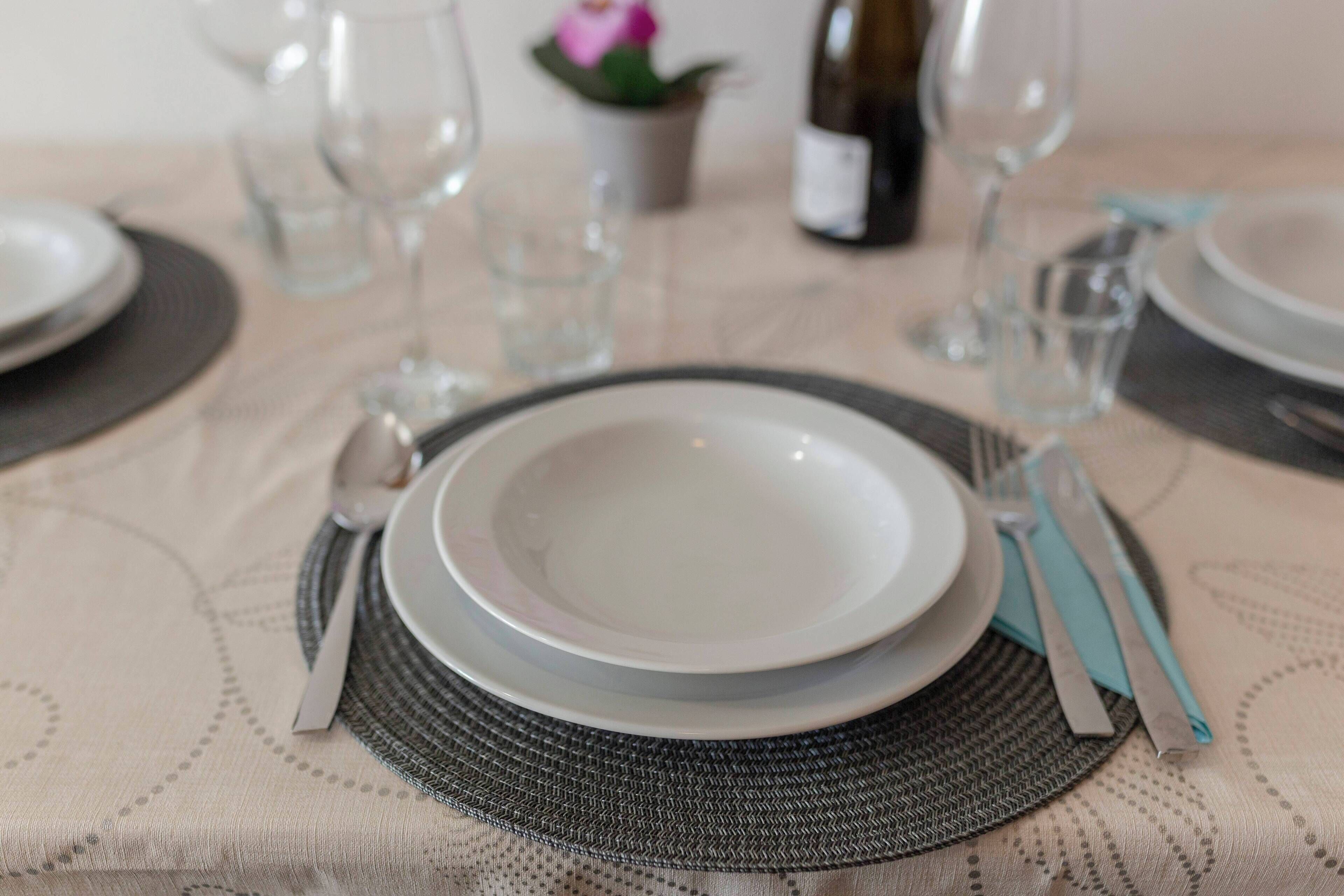 Mesa posta com pratos, talheres e uma garrafa de vinho, indicando uma área de refeições.