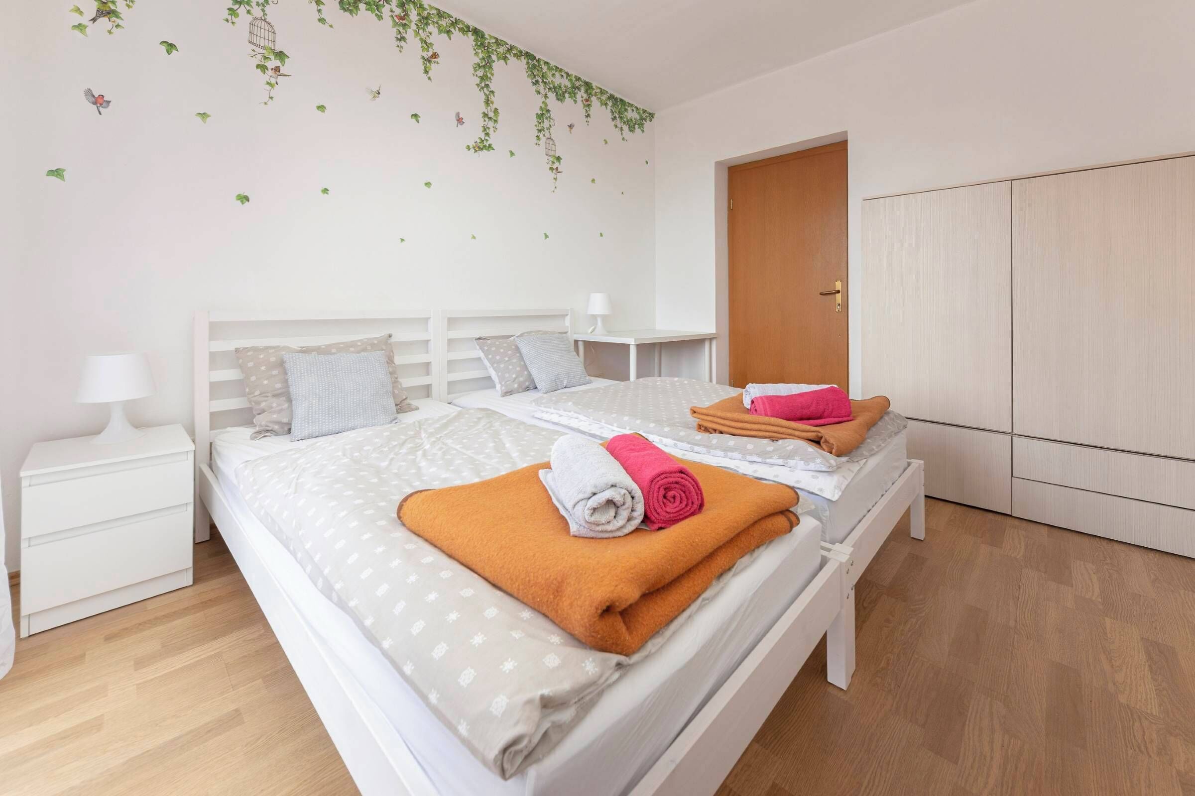 A neatly made bed with a white headboard, a bedside table with a lamp, and a wardrobe in a well-lit room.