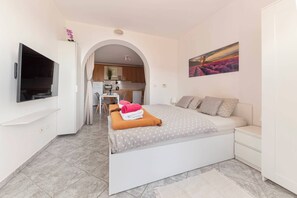 Quarto moderno com cama, televisão, quadro e vista para a cozinha.