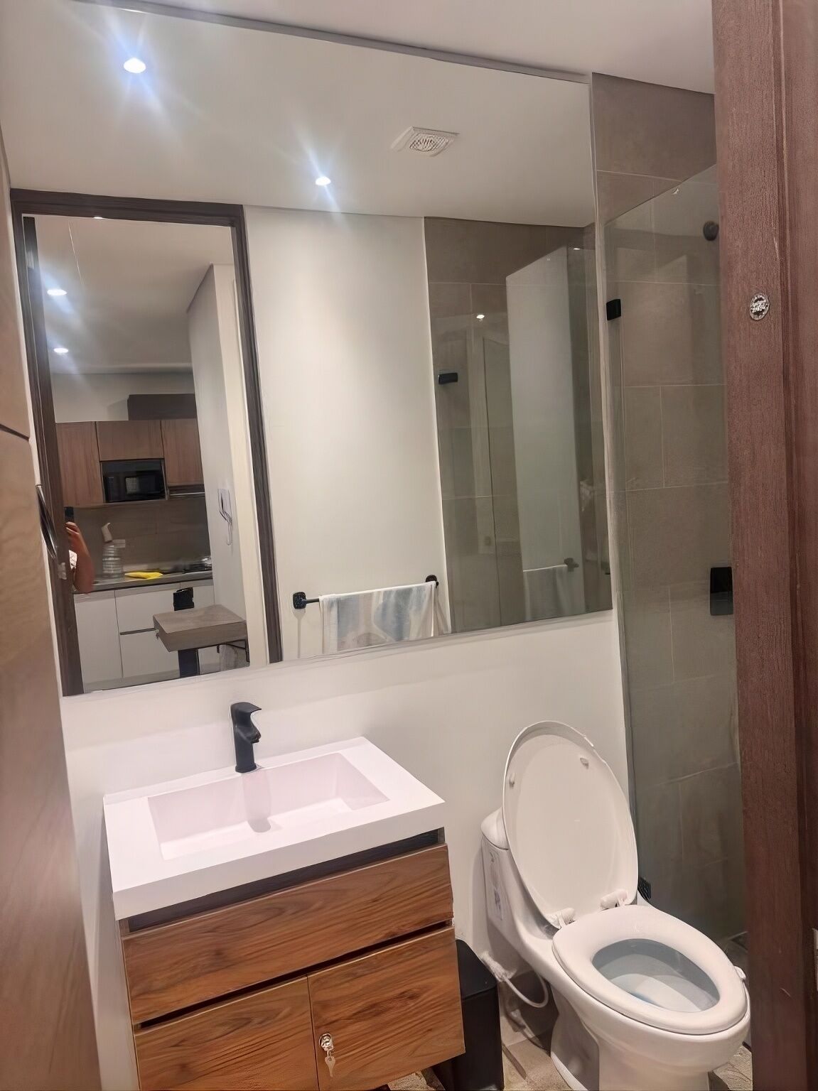 A modern bathroom with a white sink, wooden vanity, a glass shower enclosure, and a toilet.