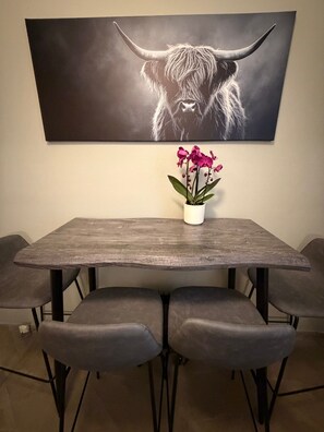 Uma sala de jantar com mesa, cadeiras, uma orquídea em vaso e uma pintura de um touro na parede.