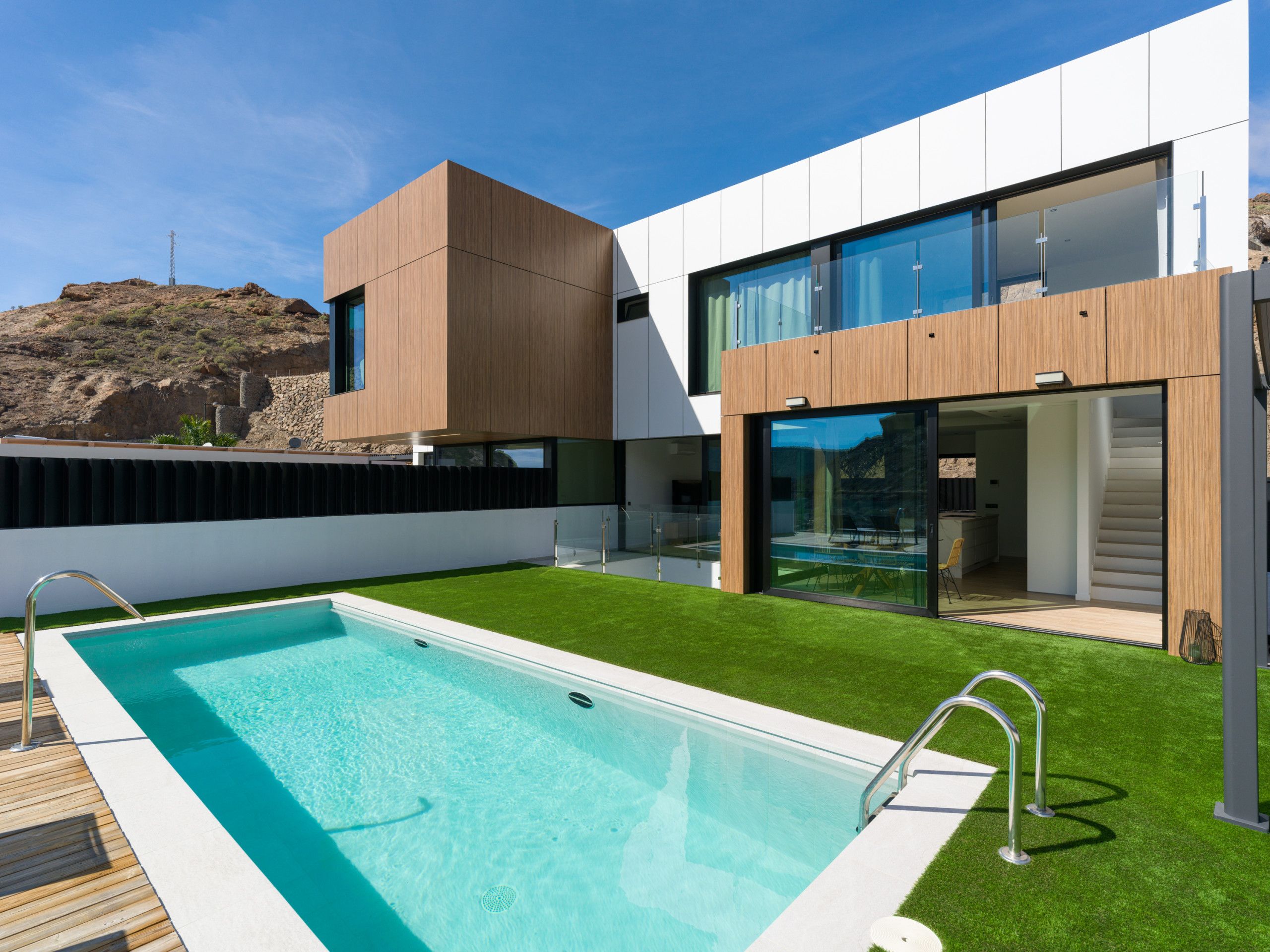 A modern house with a swimming pool, a stone wall, and a clear blue sky.