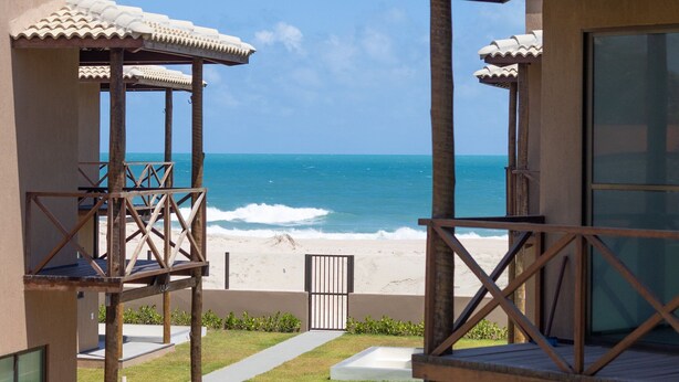A beachfront property with a covered outdoor area, a pathway leading to the beach, and a view of the ocean.