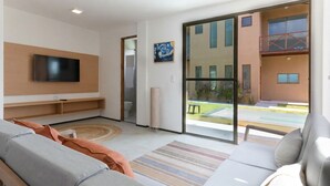 A modern living room with a flat-screen TV, a sofa, a coffee table, and a large sliding glass door leading to an outdoor area.