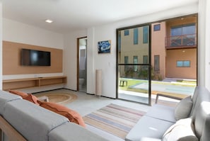 Una sala de estar moderna con una televisión de pantalla plana, un sofá, una mesa de centro y un amplio ventanal corredera que da a un área exterior.