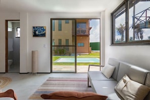 A modern living room with a sofa, a large window, and a sliding glass door leading to a pool. - Beachfront Duplex #A6 - Aquiraz By Carpediem (Aquiraz)