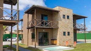 A modern two-story building with a balcony, a swimming pool, and a green fence in the background.