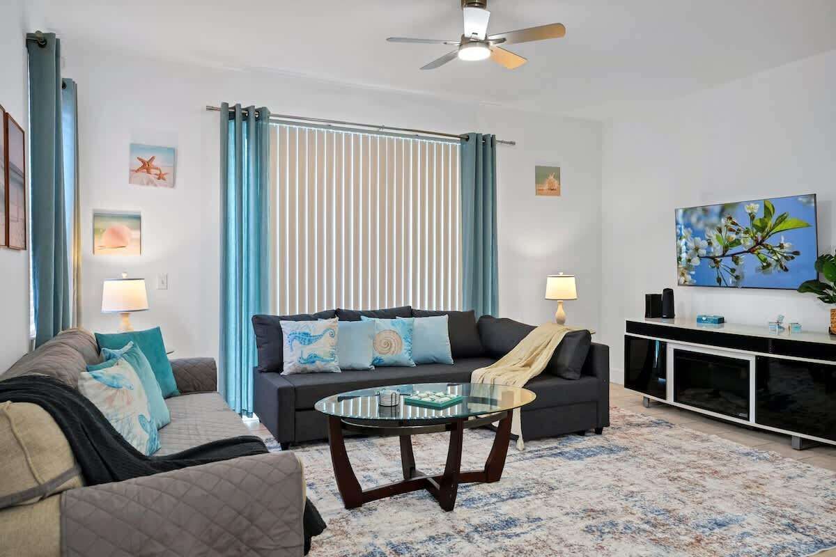 A living room with a sofa, armchair, and coffee table. There is a ceiling fan, a TV, and a plant on a cabinet.
