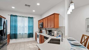 A modern kitchen with wooden cabinets, a stainless steel microwave, and a large island with a sink. - Family Getaway Near Disney - 3BR and Pool Access (Kissimmee)