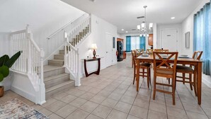 A spacious living area with a staircase, a dining table with chairs, and a kitchen in the background. - Family Getaway Near Disney - 3BR and Pool Access (Kissimmee)