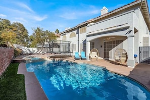 Une piscine à l’eau d’un bleu cristallin, entourée d’un patio aménagé avec des chaises longues et un espace salon couvert.