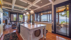 A spacious kitchen with a large island, wooden flooring, and a view of the ocean. - Tewesi Manor | Historic Tahoe Lakefront w/ Private Pier (Carnelian Bay)