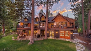 A multi-story log cabin with a stone foundation, large windows, and a stone pathway leading to the entrance. - Tewesi Manor | Historic Tahoe Lakefront w/ Private Pier (Carnelian Bay)