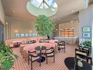 Ein großzügiger Loungebereich mit einem zentralen Baum, verschiedenen Sitzgelegenheiten und einer Bar im Hintergrund.