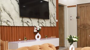 Un soggiorno moderno con parete in marmo, televisore a schermo piatto, rivestimenti in legno, un tavolino consolle bianco e divani in pelle trapuntata.