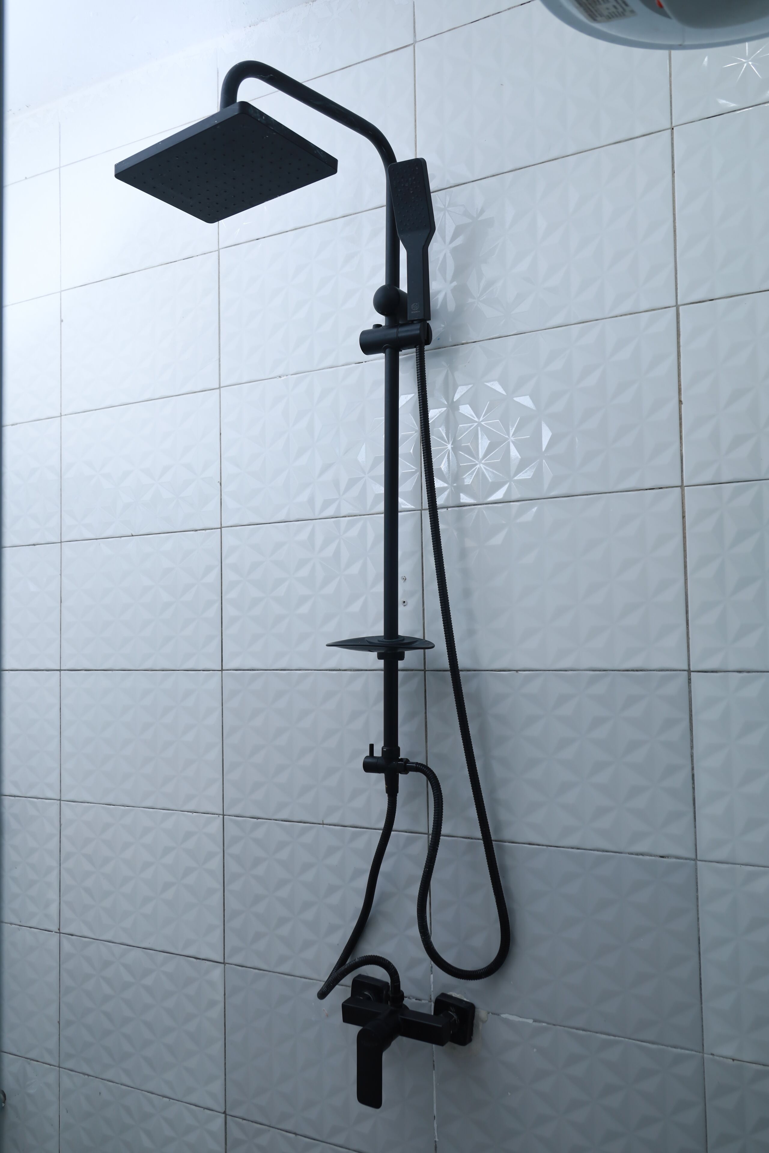 Een zwarte douchekop bevestigd aan een witte betegelde muur met een geometrisch patroon.