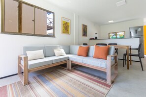 A modern living room with a sectional sofa, a dining table with chairs, a kitchen area, and artwork on the walls.