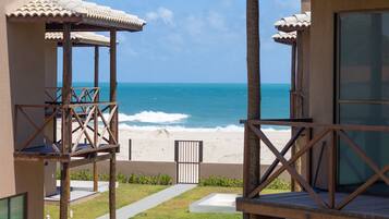 A beachfront property with a covered outdoor area, a pathway leading to the beach, and a view of the ocean.