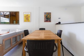 Un coin repas avec une table en bois et des chaises noires, un canapé et deux tableaux accrochés au mur.