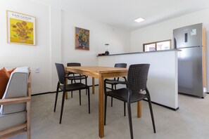 Una cocina compacta con una mesa de madera y cuatro sillas, un refrigerador y una licuadora sobre la encimera.