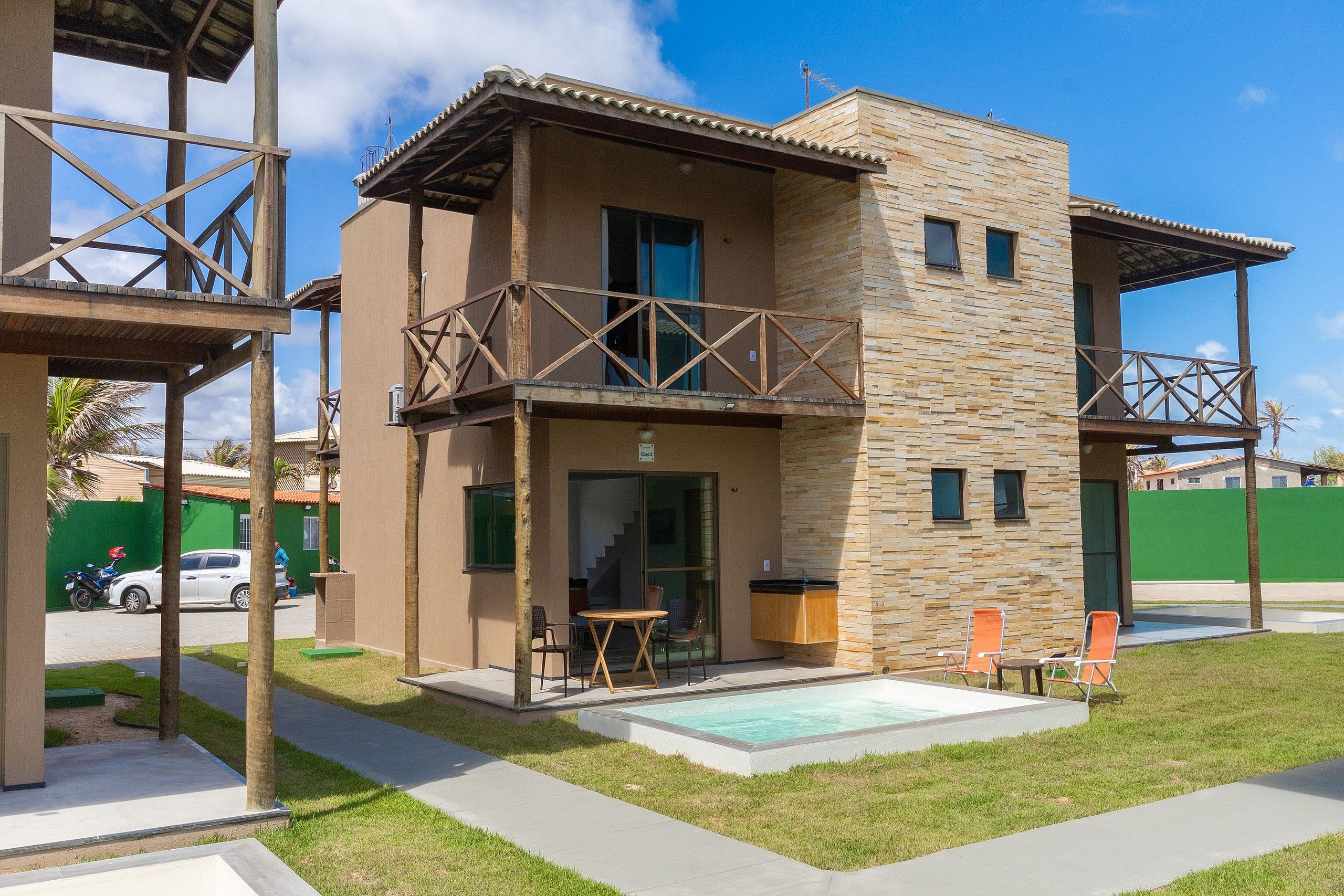A two-story building with a balcony, a swimming pool, and a green fence in the background.