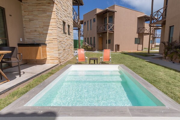 Una piscina con agua cristalina azul, rodeada por un área verde y un edificio de fachada de ladrillo.