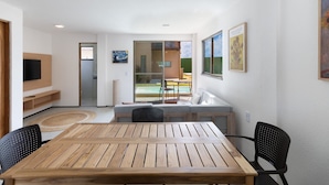Ein modernes Wohnzimmer mit Holztisch und -stühlen, einer Couch und einem Fernseher. Eine Schiebetür aus Glas führt zu einem Balkon mit einem Pool.