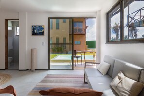 Ein modernes Wohnzimmer mit einer Couch, einem gemusterten Teppich und einer Glastür, die auf einen Balkon mit Blick auf ein Gebäude und Palmen führt.