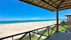 Blick auf einen Strand von einer überdachten Terrasse mit Holzgeländer.