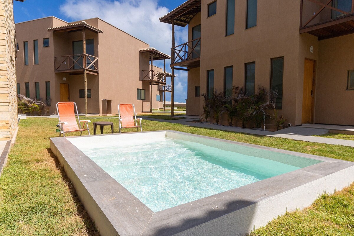 Une piscine entourée d’une pelouse, avec un bâtiment doté de balcons et d’une porte.