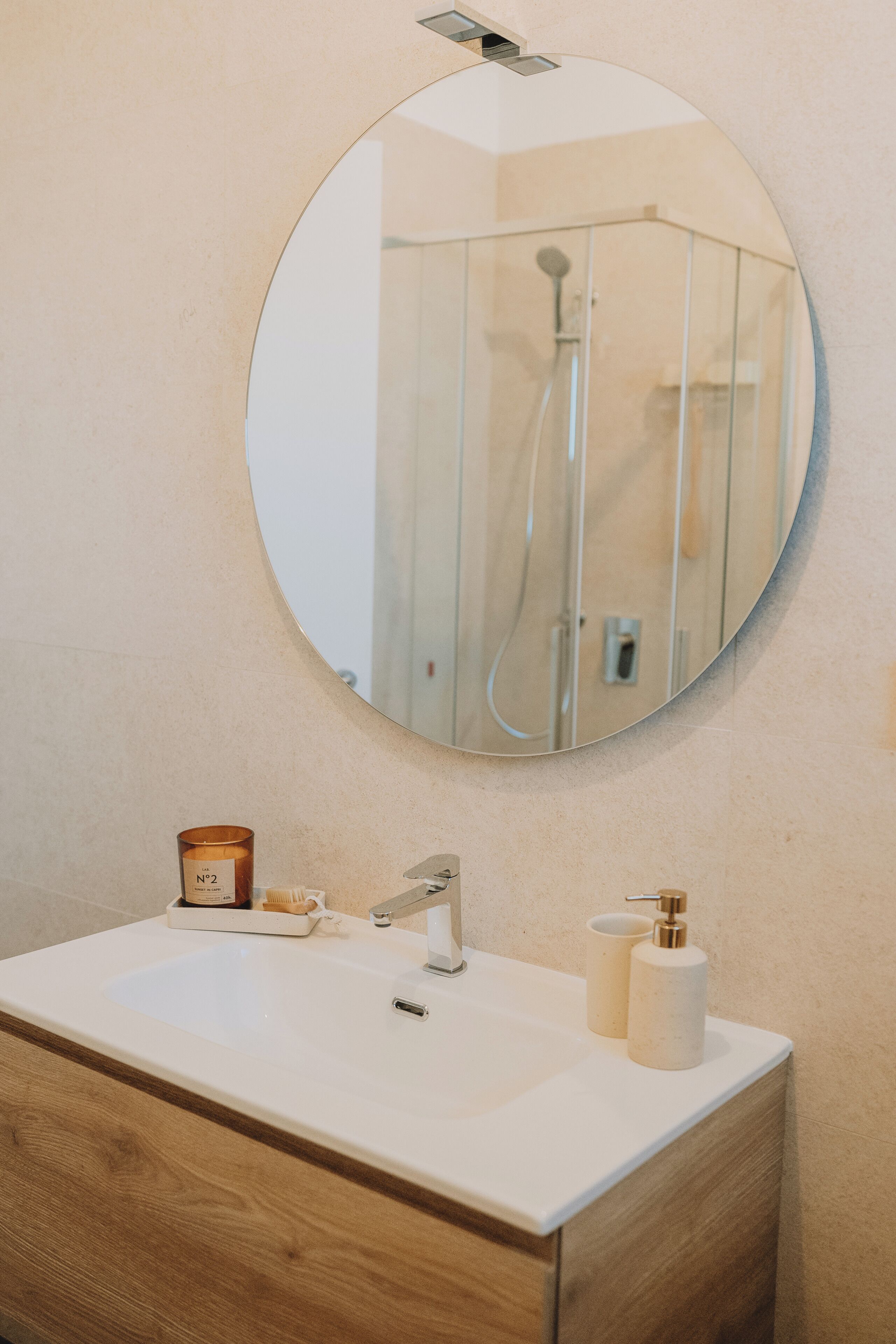Un baño con un espejo redondo, un lavabo, un armario de madera y artículos de aseo.