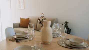 A dining table set with plates, glasses, and cutlery, a vase with dried flowers, and a sofa in the background.