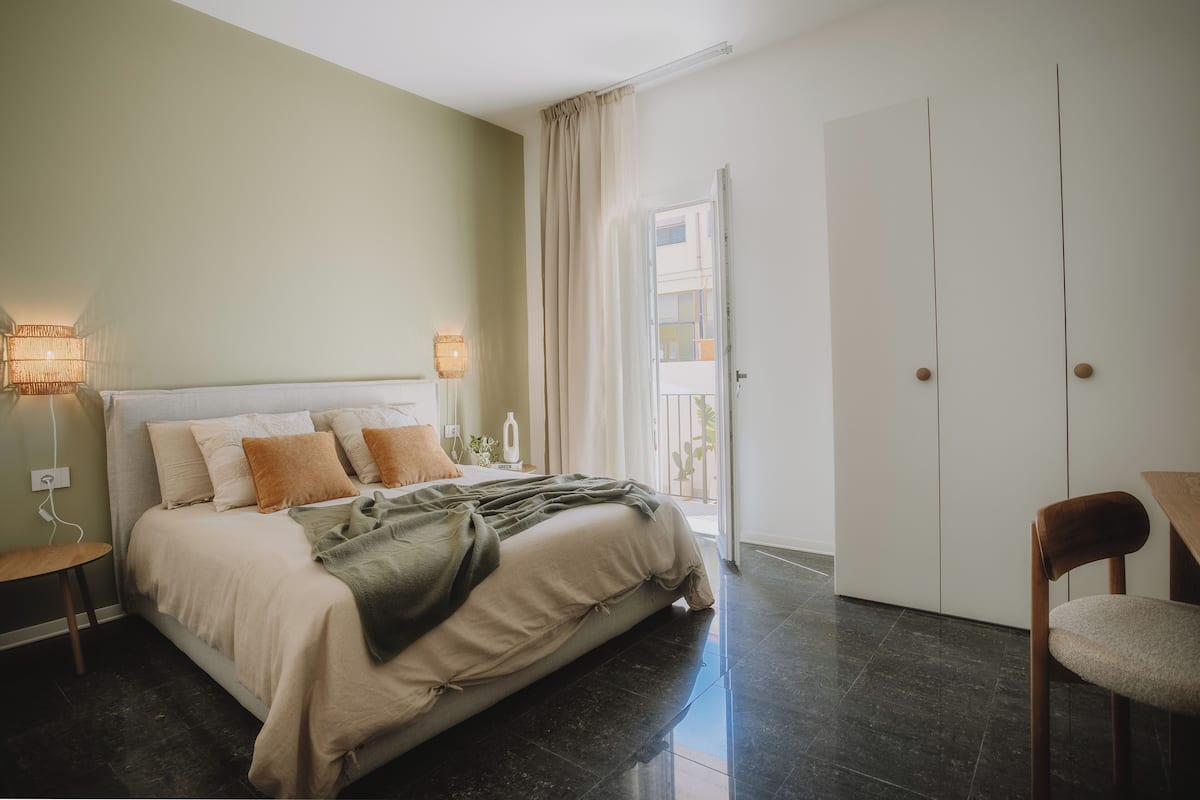 Un dormitorio con cama, lámparas de noche, una silla y una puerta que da a un balcón.