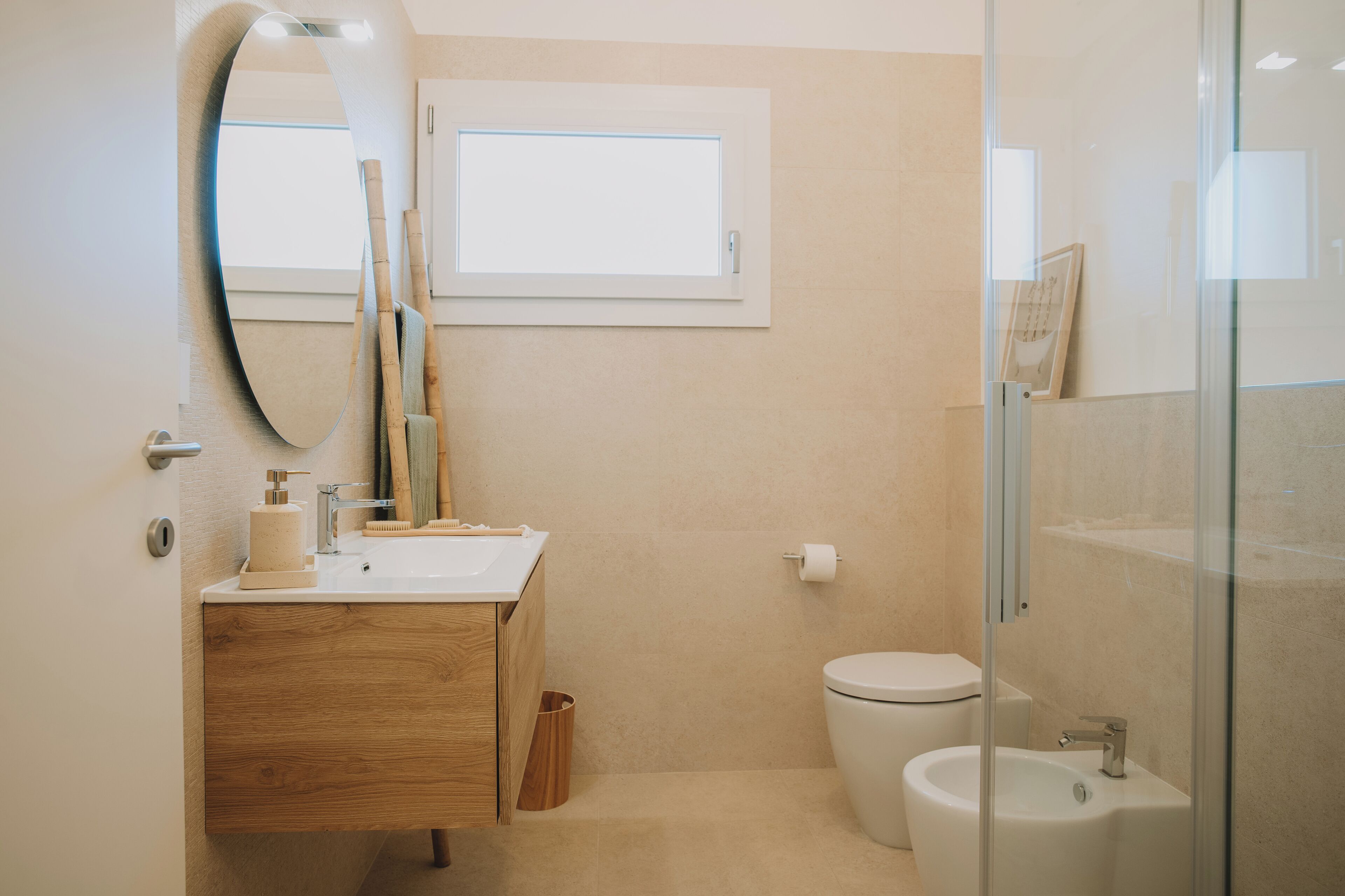 Un baño con tocador de madera, inodoro, bidé, espejo y ventana.