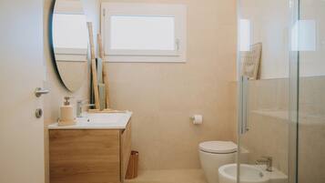 Un baño con tocador de madera, inodoro, bidé, espejo y ventana.