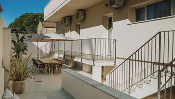 Ein Gebäude mit Balkon, Außenbestuhlung und einer Treppe.