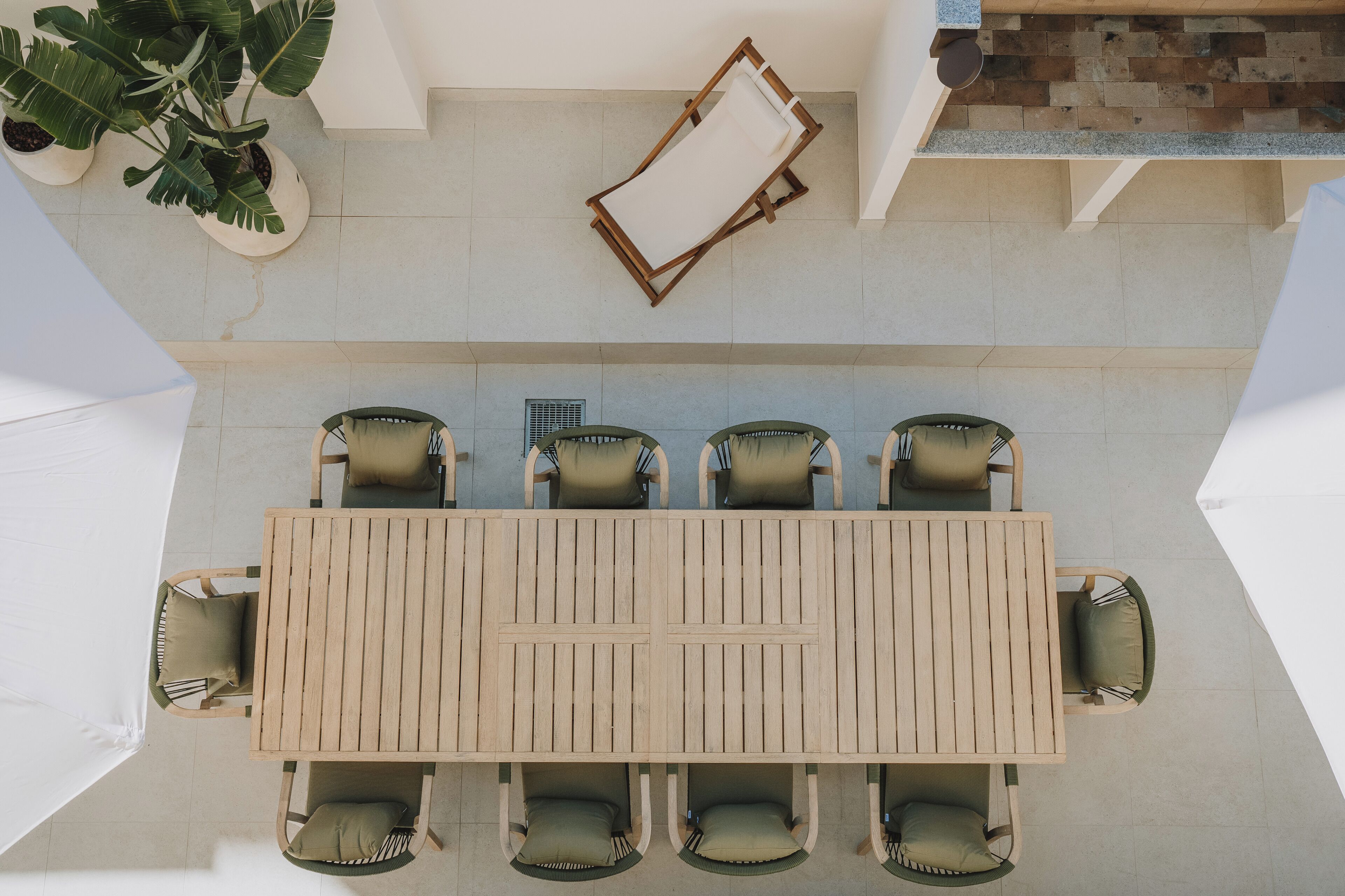 Vista cenital de una mesa de madera con seis sillas, rodeada de plantas en macetas, en un entorno exterior.