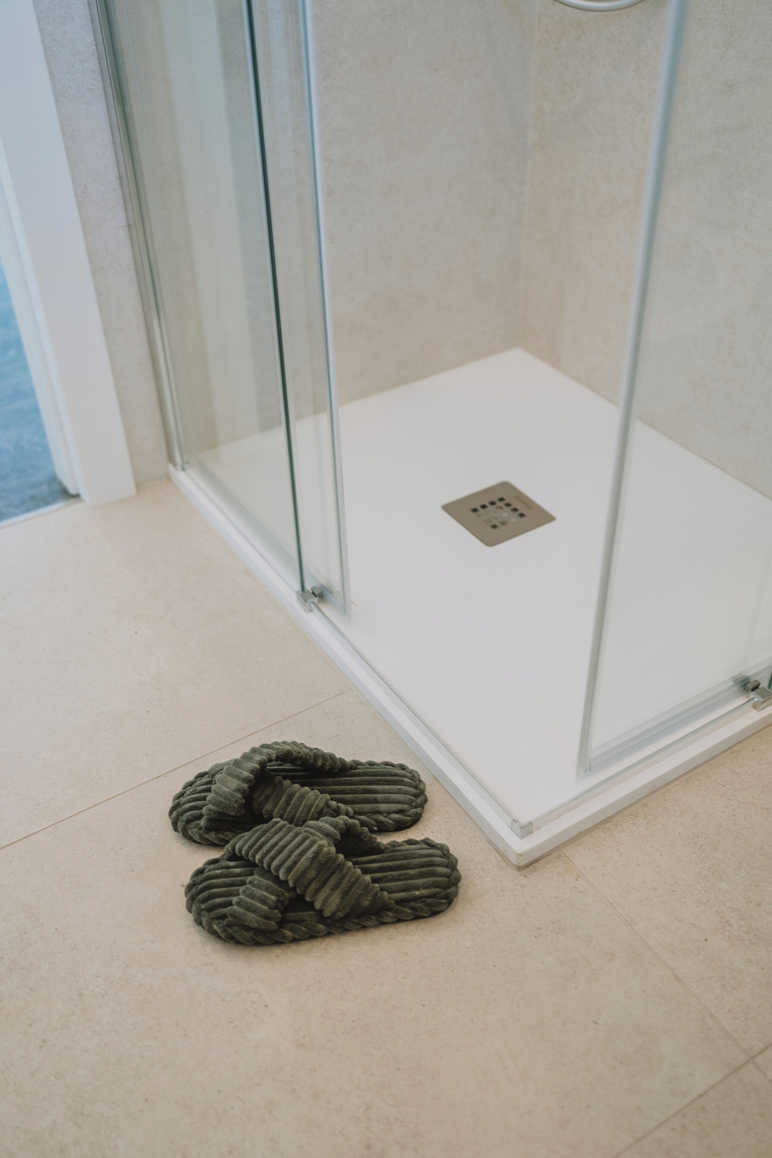 A glass-enclosed shower area with a white floor and a visible drain.