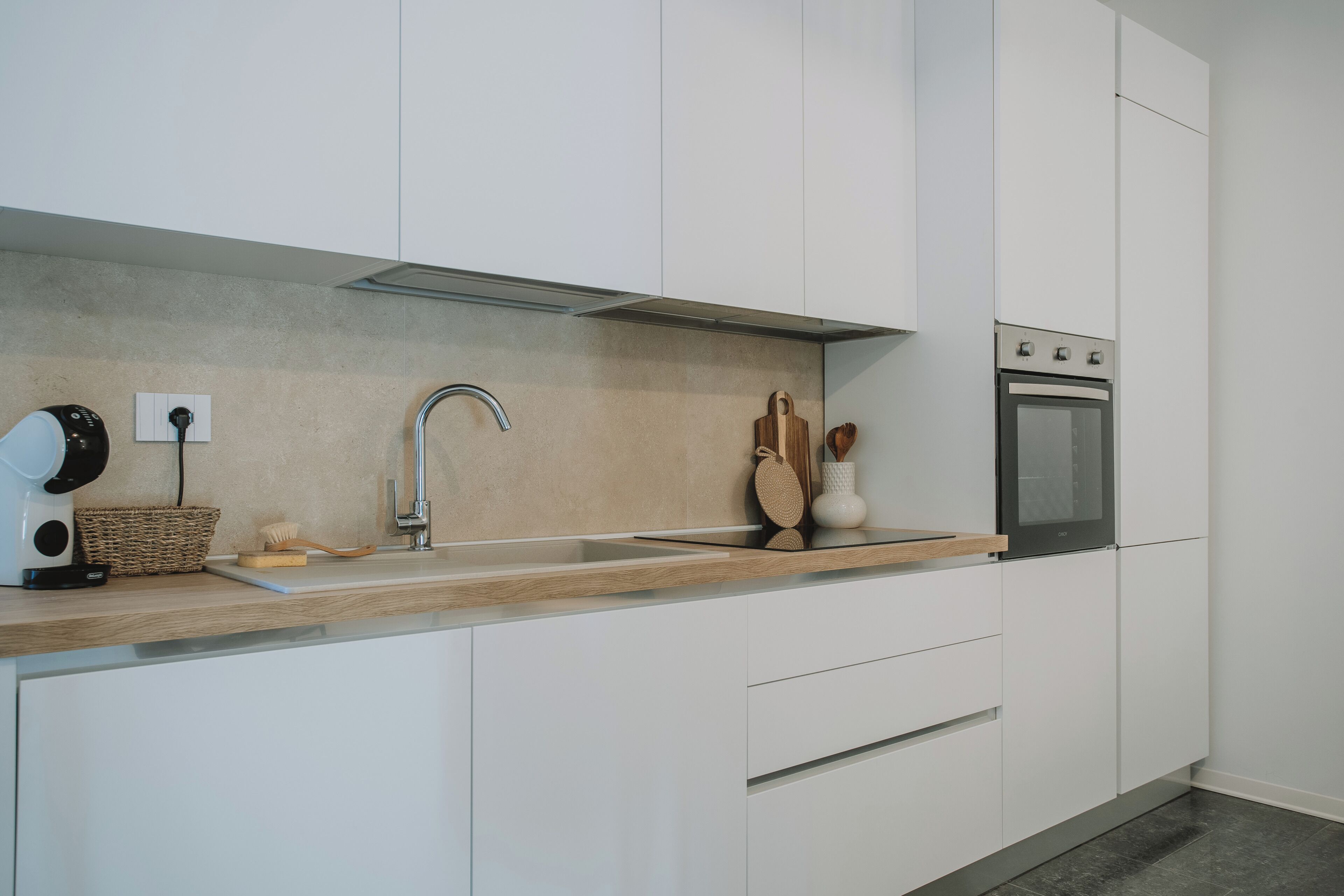 Una cucina moderna con mobili bianchi, forno in acciaio inossidabile e piano di lavoro in legno.