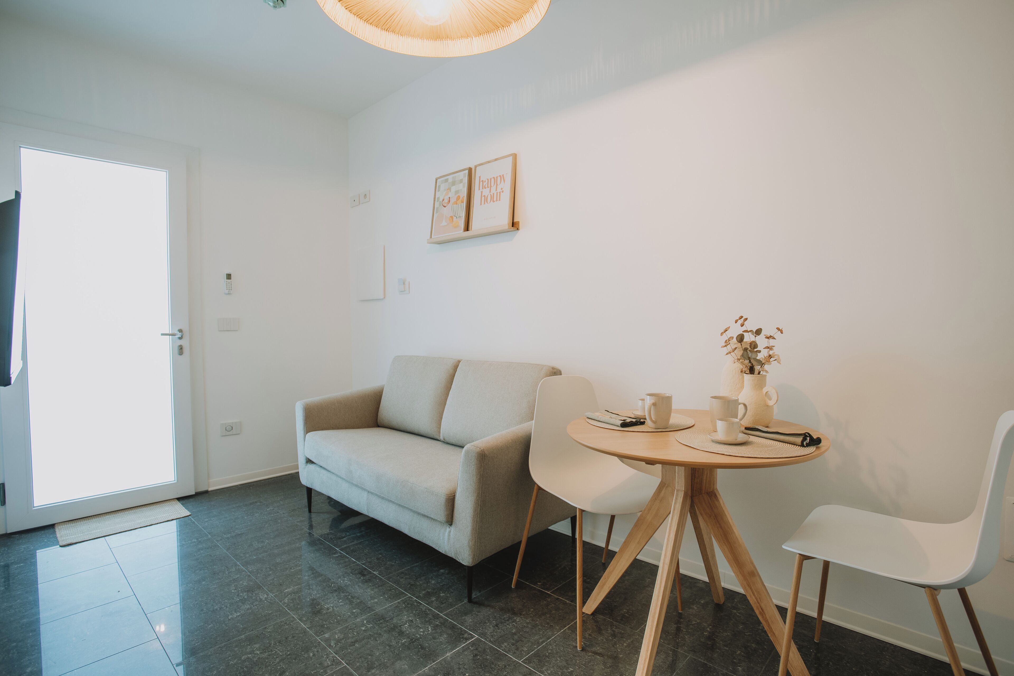 Ein modernes Wohnzimmer mit einer Couch, zwei Sesseln, einem kleinen runden Tisch mit einer Vase und einem gerahmten Bild an der Wand.