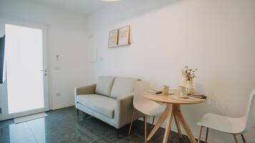 Ein modernes Wohnzimmer mit einer Couch, zwei Sesseln, einem kleinen runden Tisch mit einer Vase und einem gerahmten Bild an der Wand.