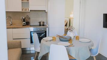 Una cocina moderna con una mesa de comedor preparada para dos personas, un horno empotrado y un televisor montado en la pared.
