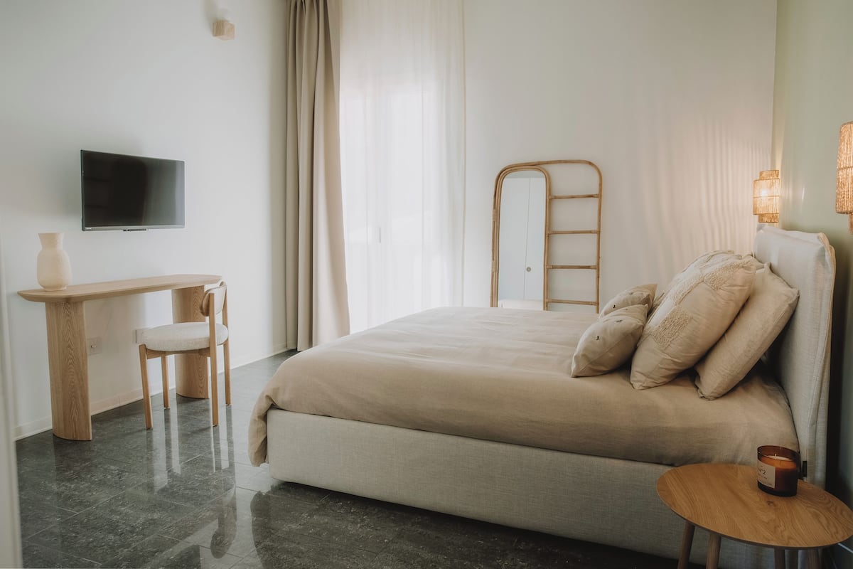 Un dormitorio con una cama, un escritorio, una silla, un televisor, una mesita de noche y una lámpara.