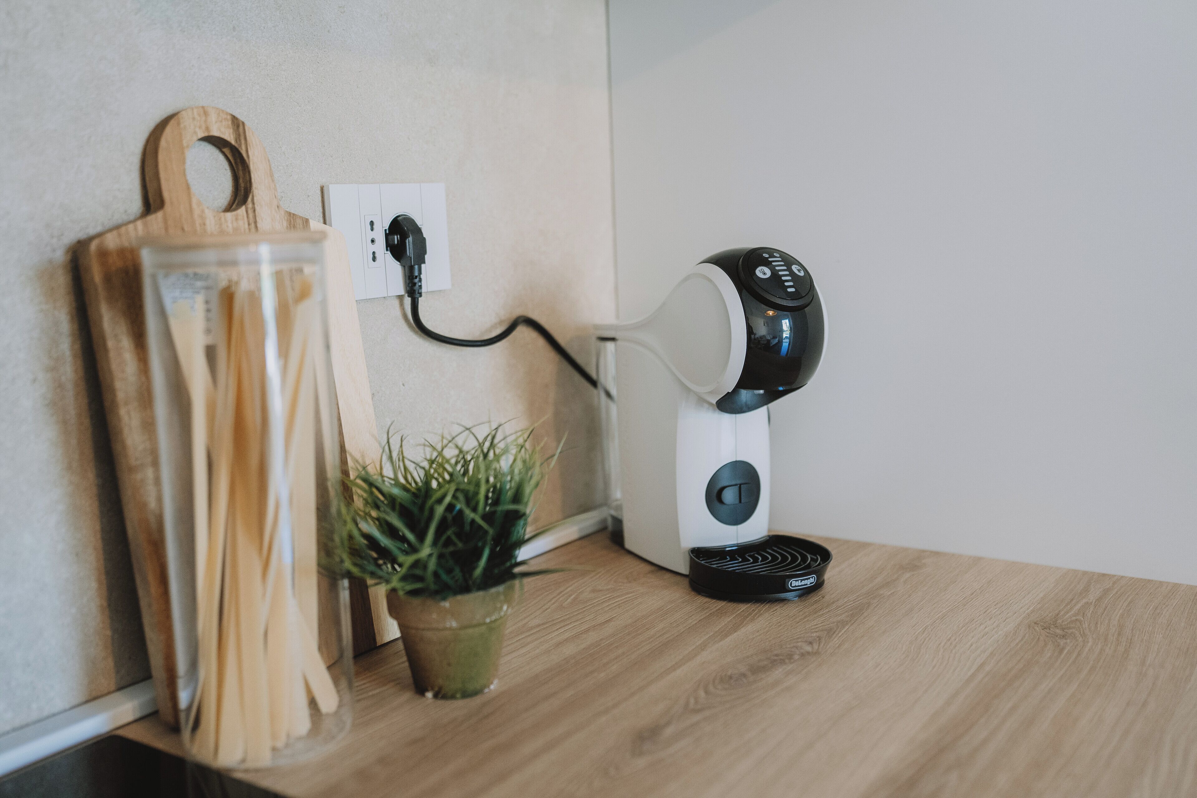 Eine Küchenarbeitsplatte mit Kaffeemaschine, Schneidebrett aus Holz und einem Topf mit Pflanze.