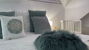 Un dormitorio con techo inclinado, tragaluz, cama con ropa de cama blanca y un almohadón gris suave.