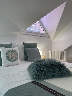 A bedroom with a sloped ceiling, a skylight, a bed with white bedding, and a fluffy gray pillow. - 6-person 2-bedroom Premium apartment panoramic sea and pool view (Sainte anne)