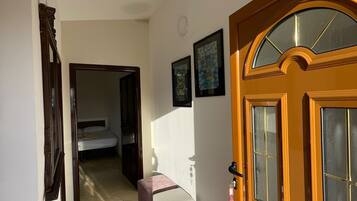 A hallway with a wooden door, a bed, and a small table.