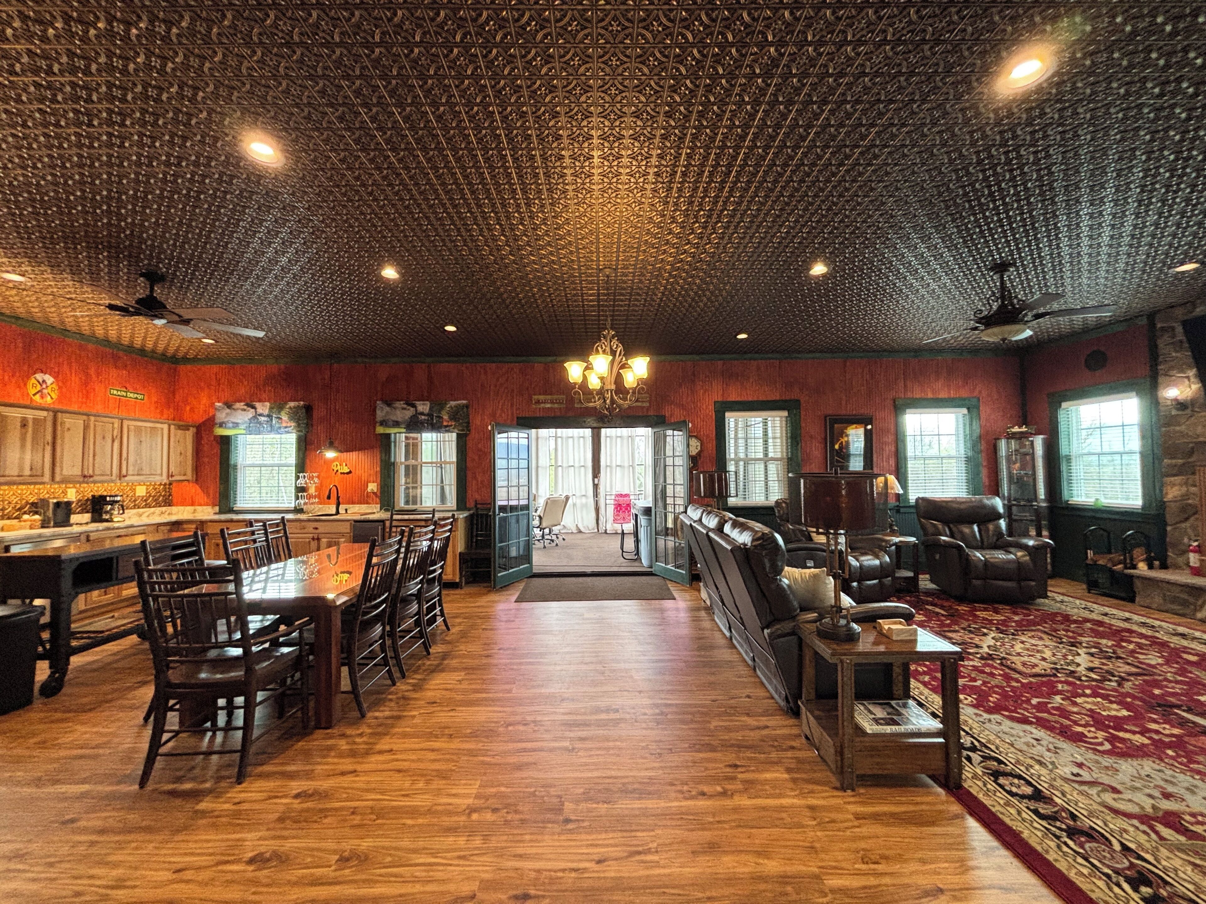 A spacious room with a wooden floor, a dining area with chairs and a table, a seating area with sofas and a rug, and a kitchen with cabinets and a counter.